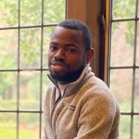 Malcom King is sitting infront of big windows, smiling at the camera.