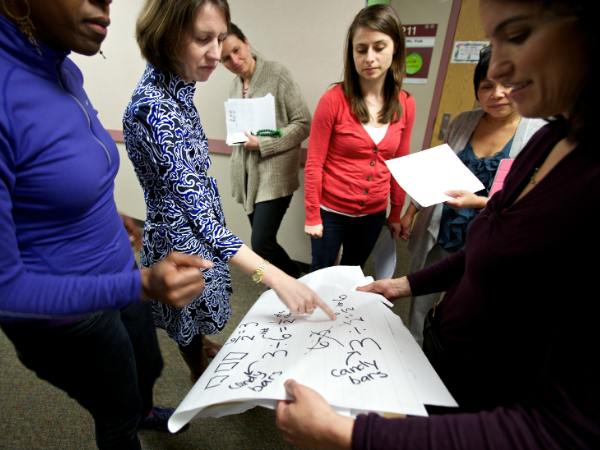 Teachers gather around a poster that has equations written on it.