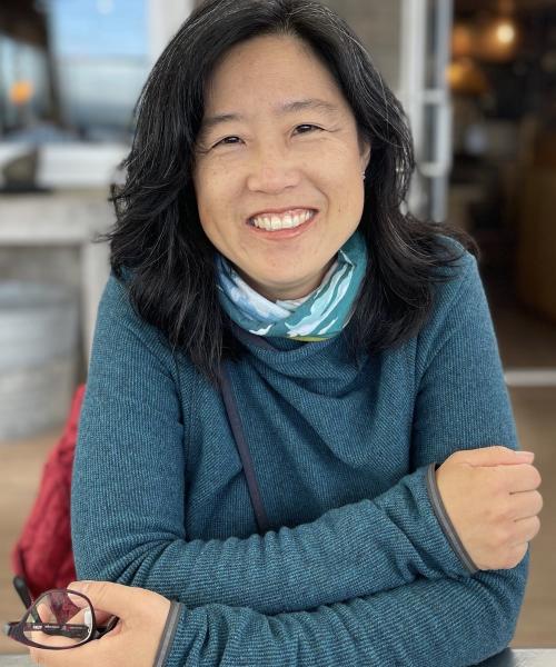 woman with shoulder-length black hair smiling, wearing a blue sweater, her arms are crossed in front of her