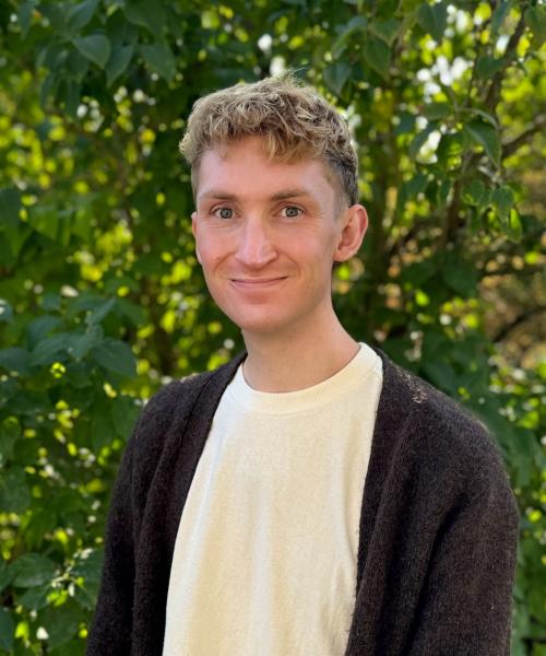 Headshot of Alec wearing cream-colored shirt and brown cardigan.