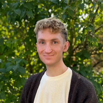 Headshot of Alec wearing cream-colored shirt and brown cardigan.