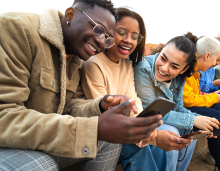 A group of multiracial youth joyfully gather to view content on their smart phones. Image source: Shutterstock.