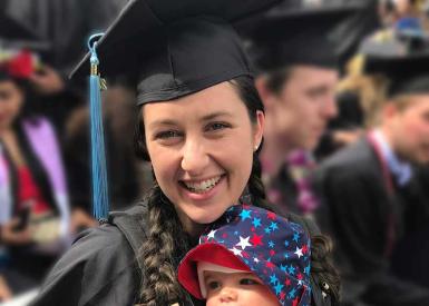 Heather White holding diploma and new born baby during graduation ceremony